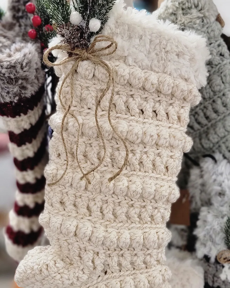 A white hand-crocheted Christmas stocking decorated with evergreen sprigs, white berries and a twine bow