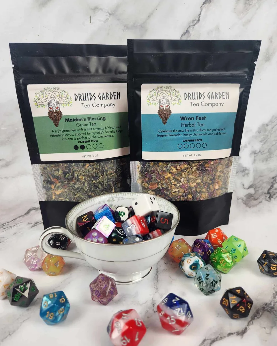 Two bags of Druids Garden loose-leaf tea beside a cup of colorful gaming dice