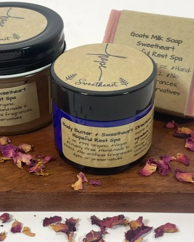 Handmade body butter, salt scrub and goat's milk soap arranged with dried rose petals