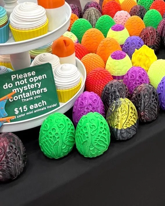 Rows of brightly colored 3D-printed sensory eggs and mystery containers on a market table