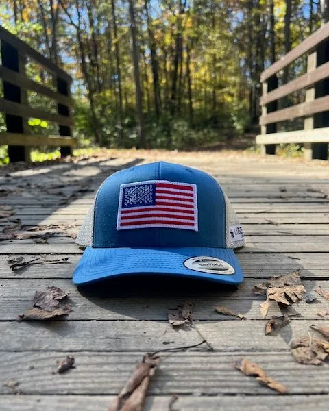 A blue trucker cap with an embroidered American flag patch on a wooden bridge