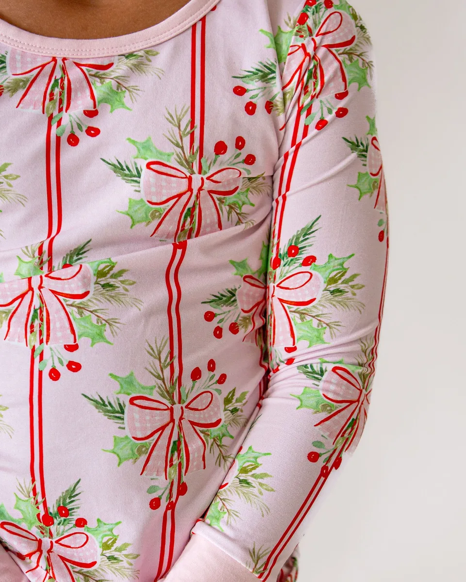 Close view of pink holiday pajamas patterned with ribbons, holly and evergreen sprigs