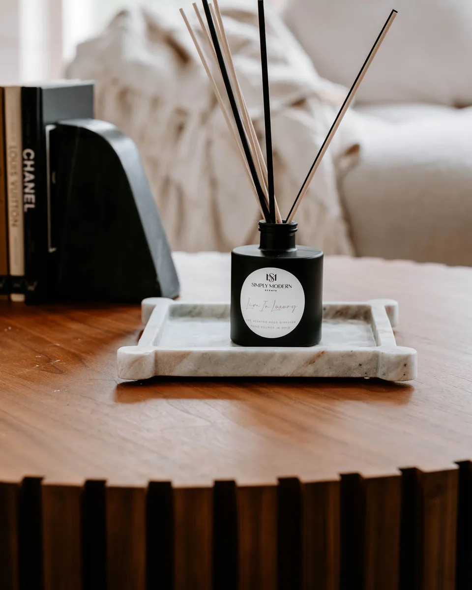 A black Simply Modern reed diffuser on a marble tray beside books