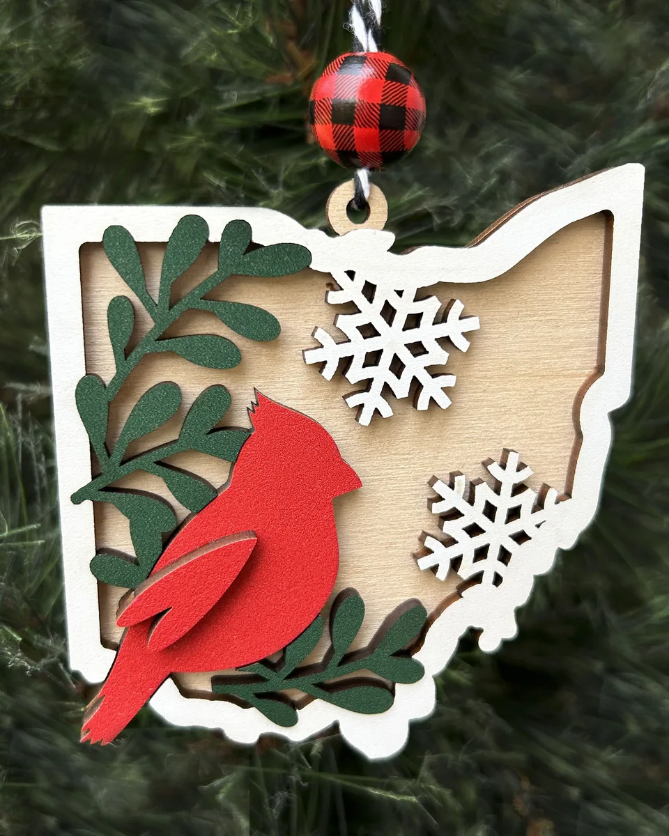 An Ohio-shaped wood ornament with a red cardinal, snowflakes and a buffalo-plaid bead