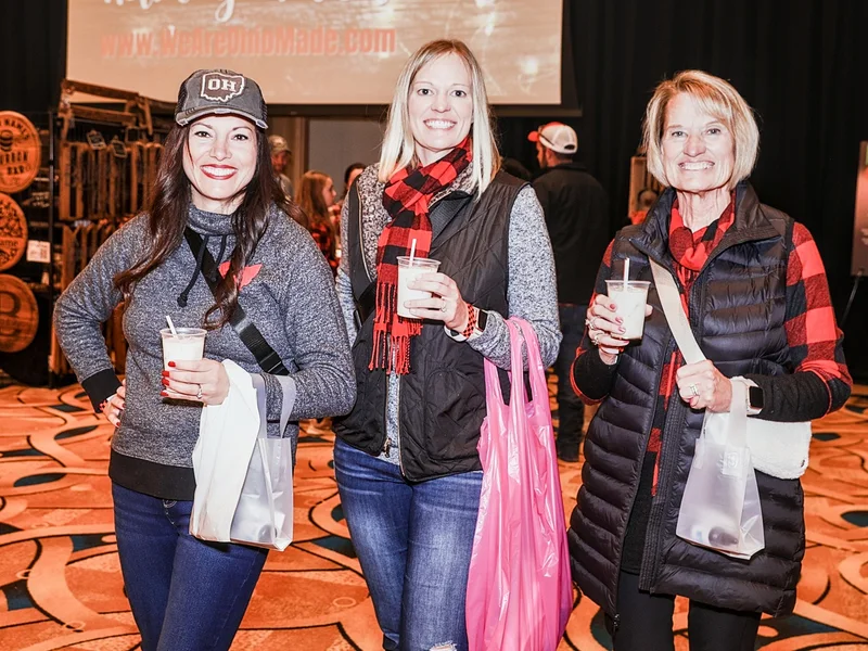 Three guests hold drinks and shopping bags in front of the Ohio Made Holiday Market screen at the 2022 Ohio Made Holiday Market.