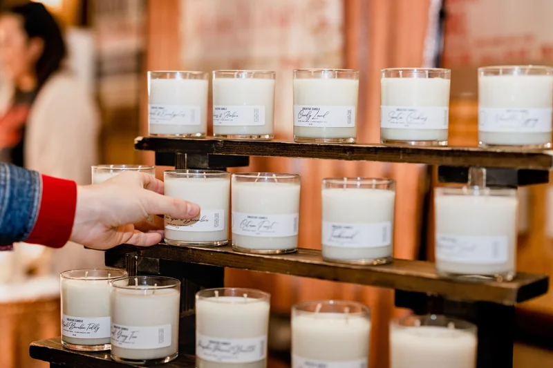 A shopper reaches for a candle on a wooden shelf of candles at the 2023 Ohio Made Holiday Market.