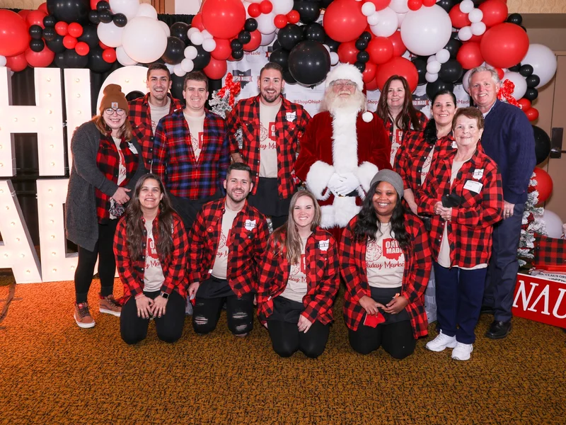 Ohio Made volunteers in red plaid kneel and stand around Santa in front of the marquee letters at the 2021 Ohio Made Holiday Market.