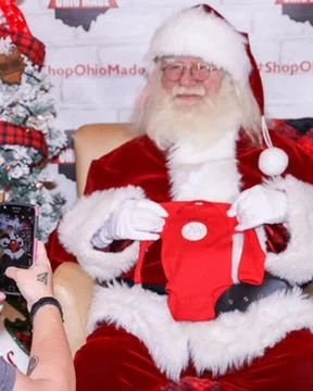 A guest takes a phone photo of Santa holding a red baby onesie.