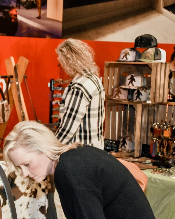 A shopper leans in to look over a display of hats and leather goods at the 2025 Ohio Made Holiday Market.