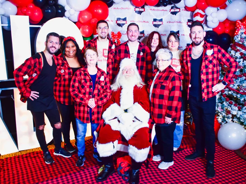 Ten Ohio Made volunteers in red plaid pose around Santa in front of the marquee letters and the Ohio Made backdrop at the 2024 Ohio Made Holiday Market.