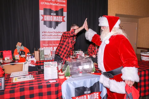 Santa gives a volunteer in a plaid shirt a high five at the raffle table.