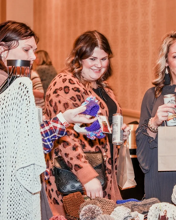 Friends laugh over drinks beside a table of hand-knit hats at the 2022 Ohio Made Holiday Market.