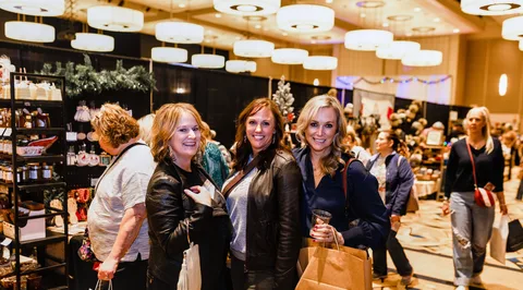 Three women smile for the camera on the market floor, one holding a drink.
