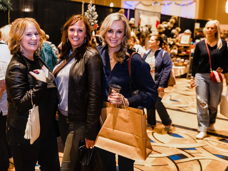 Three guests smile with kraft shopping bags in the main hall at the 2023 Ohio Made Holiday Market.