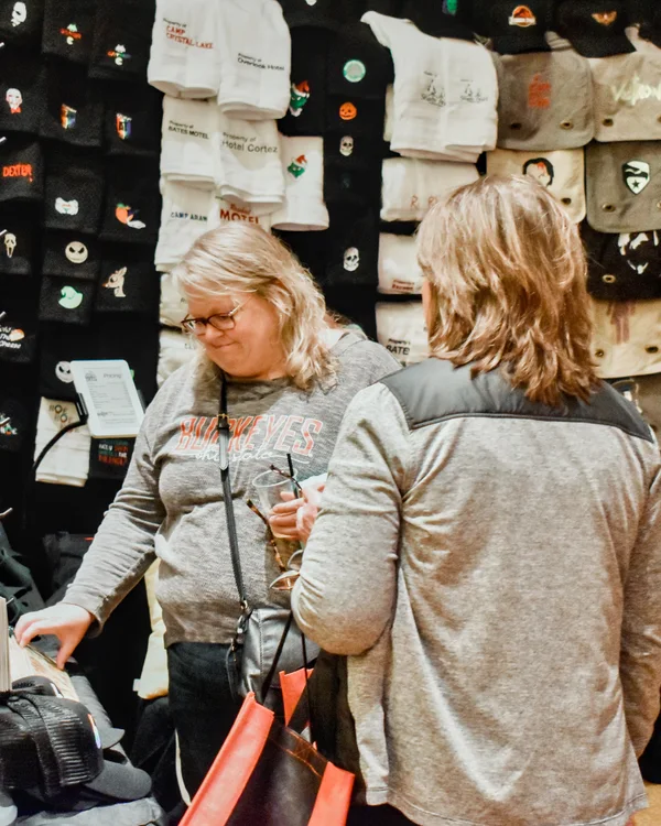 Two guests browse a wall of hats and shirts at a maker booth at the 2023 Ohio Made Holiday Market.