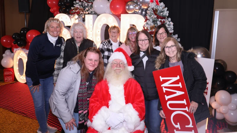 A group poses with Santa beside a Naughty sign.