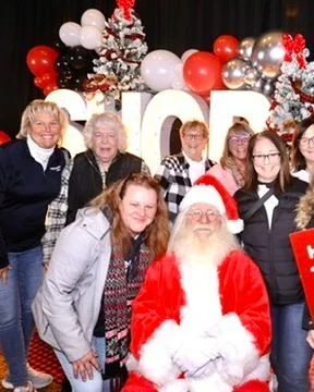 A group poses with Santa beside a Naughty sign.