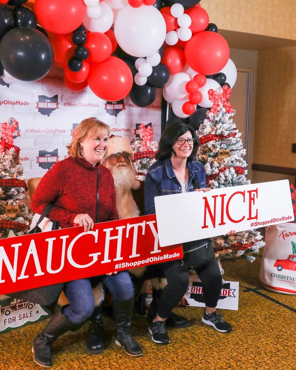 Two guests pose with Naughty and Nice signs at the 2021 Ohio Made Holiday Market photo wall.
