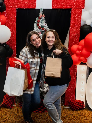 Two shoppers hold shopping bags in front of giant lit OH IO letters and a balloon arch.