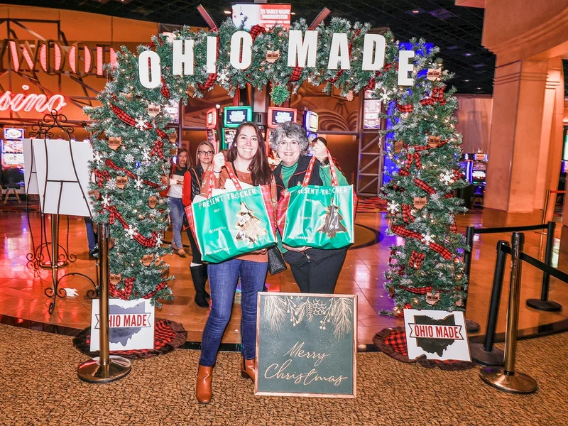 Two shoppers with green tote bags pose under the Ohio Made garland arch at the Ohio Made Holiday Market.