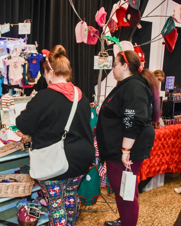 Shoppers with tote bags browse a booth of handmade baby clothes at the 2025 Ohio Made Holiday Market.