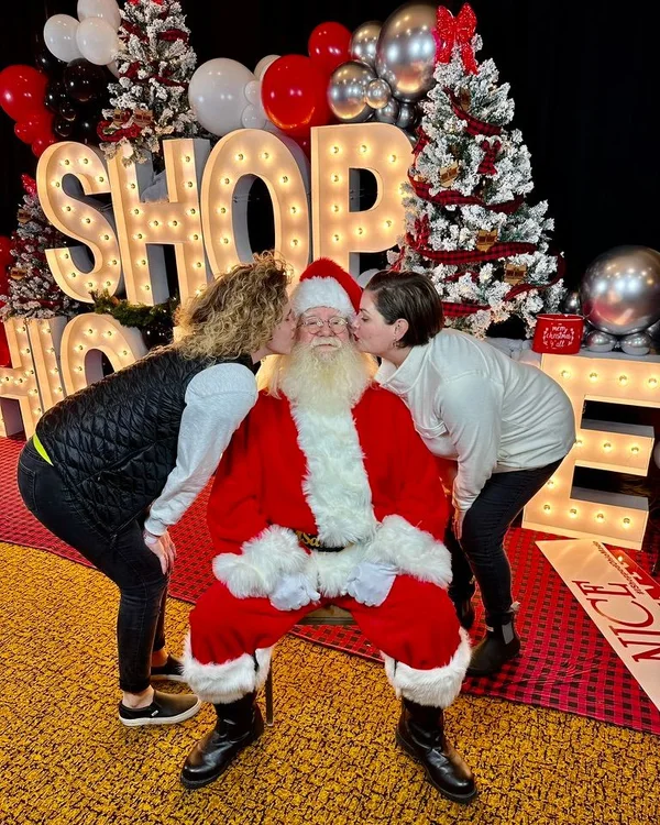 Santa with two shoppers kissing his cheeks.