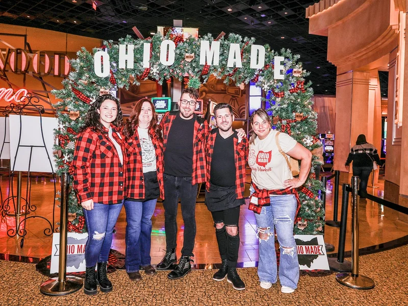 Five Ohio Made volunteers in red plaid pose together under the garland Ohio Made arch at the 2022 Ohio Made Holiday Market.