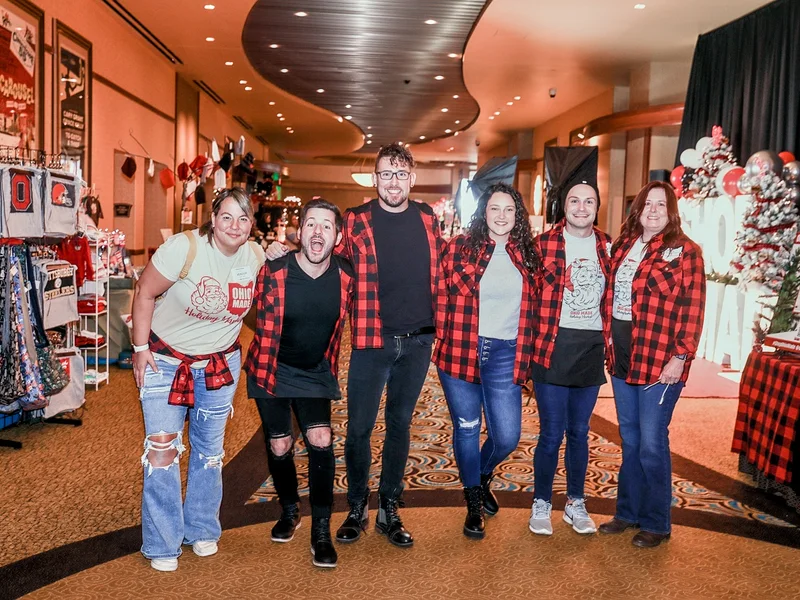 Six Ohio Made volunteers in red plaid and Ohio Made shirts pose together in a market aisle at the 2022 Ohio Made Holiday Market.