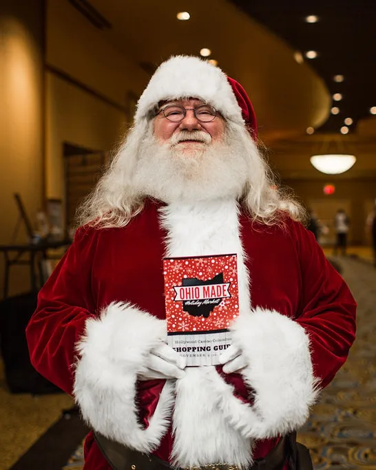 Santa smiles and holds a shopping guide in a hotel hallway.