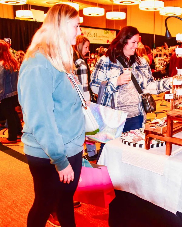 Two shoppers with drinks browse handmade gifts at the 2024 Ohio Made Holiday Market.