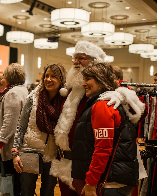 Santa poses with two shoppers while the market continues behind them.