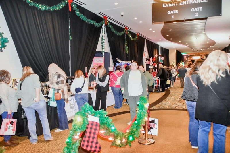 Shoppers walk a wide aisle toward the event entrance signs, past booths and a garland-wrapped rope line, at the 2025 Ohio Made Holiday Market.