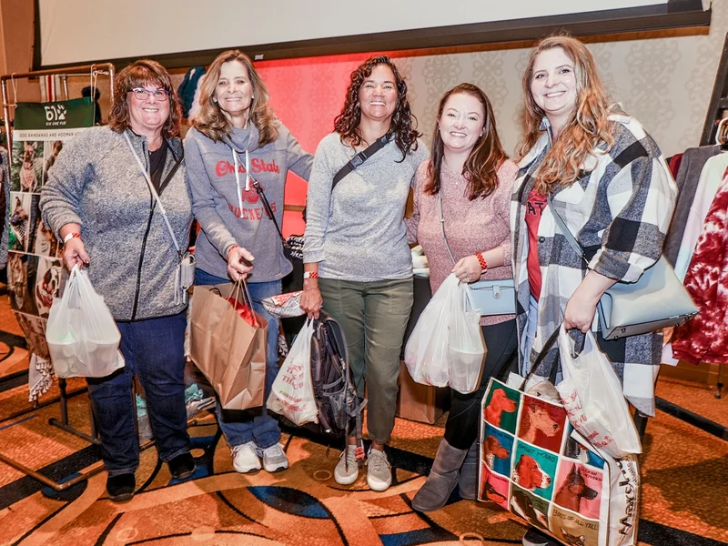 Five guests with shopping bags in front of a clothing rack at the 2022 Ohio Made Holiday Market.