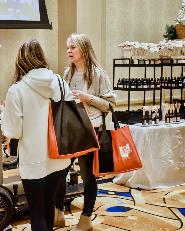 Two shoppers with tote bags stop to talk at the 2023 Ohio Made Holiday Market.