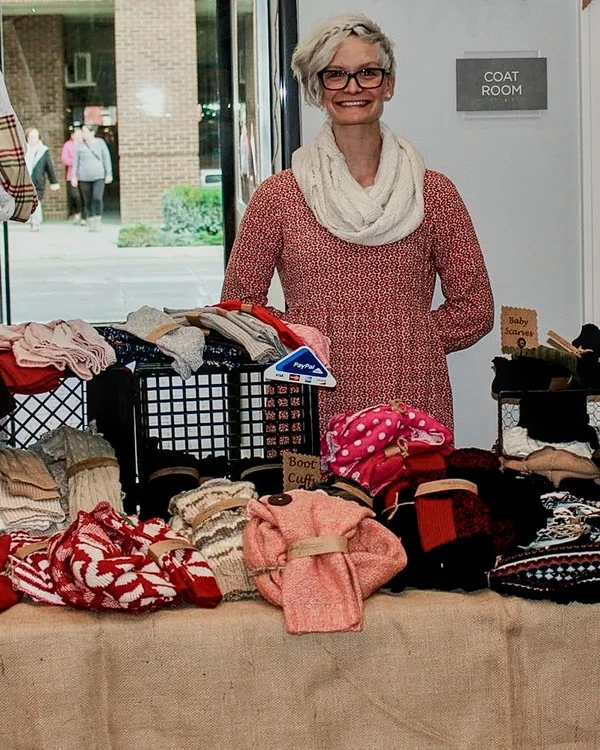 A smiling person stands behind a table of scarves and knit hats at the 2016 Ohio Made Holiday Market.