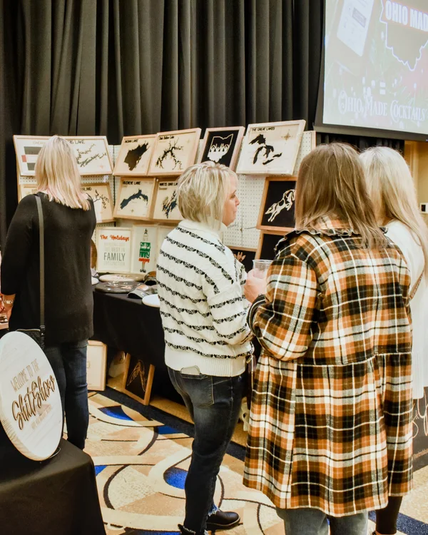 Shoppers in plaid look over engraved wooden signs at the 2023 Ohio Made Holiday Market.
