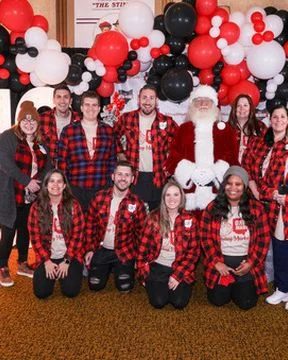 Volunteers in plaid kneel and stand around Santa in front of the marquee letters.