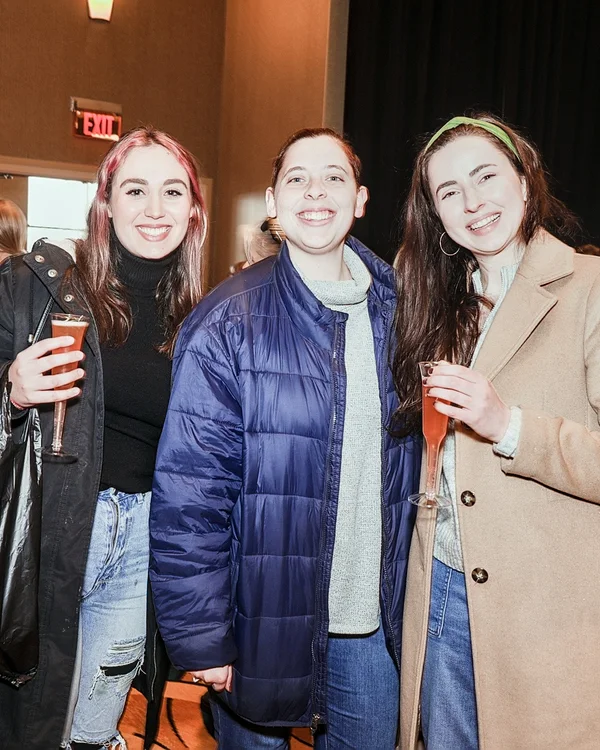 Three friends with drinks smile together near an exit door at the 2022 Ohio Made Holiday Market.