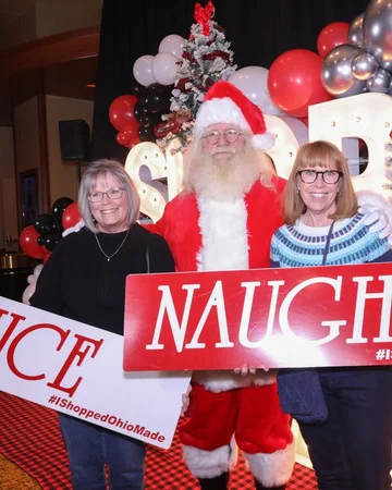 Two shoppers hold Nice and Naughty signs beside Santa.
