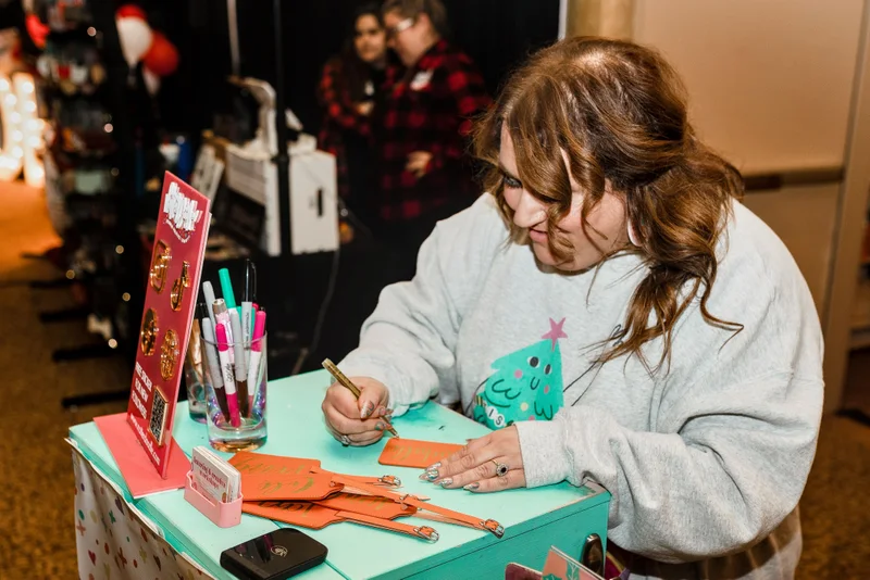 A maker personalizes a leather luggage tag at her cart at the 2023 Ohio Made Holiday Market.