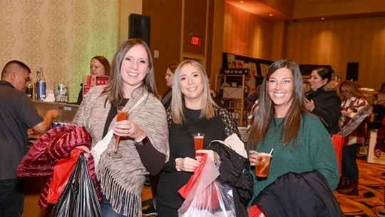 Three friends hold shopping bags and drinks.
