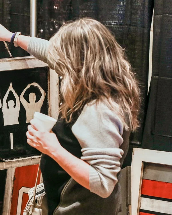 A shopper with a cup reaches for a wooden Ohio sign at the 2022 Ohio Made Holiday Market.