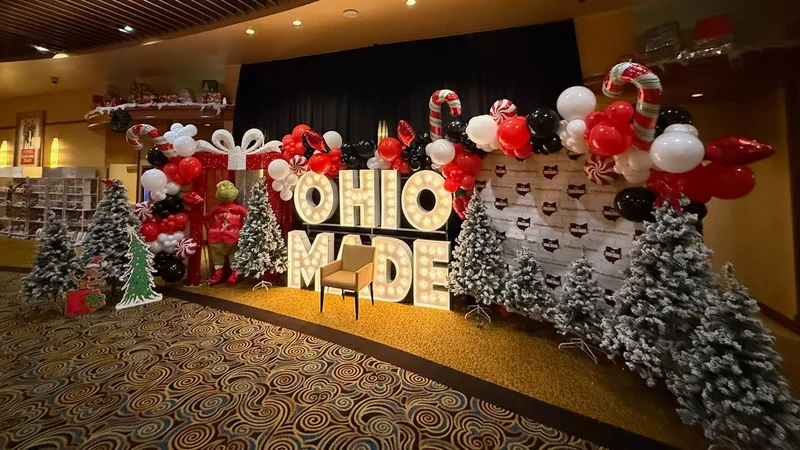 A wide holiday photo wall with the Ohio Made marquee letters, balloons and flocked trees.