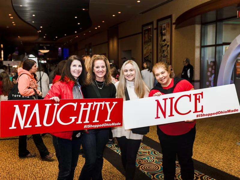 Four guests hold Naughty and Nice signs in the hall at the 2023 Ohio Made Holiday Market.